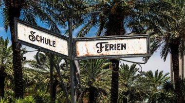 Almanca 'nın iki farklı yönünü gösteren işaret direği olan bir resim. Bir yön tatilleri gösterir, diğeri okulu gösterir..