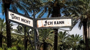 An image with a signpost pointing in two different directions in German. One direction points to I can, the other points to resignation. clipart