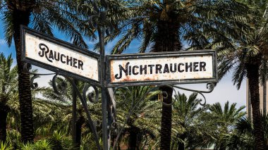Almanca 'nın iki farklı yönünü gösteren işaret direği olan bir resim. Bir yön sigara içmeyenleri, diğeri sigara içenleri gösteriyor..