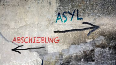 Almanca 'nın iki farklı yönünü gösteren işaret direği olan bir resim. Bir yön sığınma, diğeri sınır dışı edilmeyi işaret ediyor..