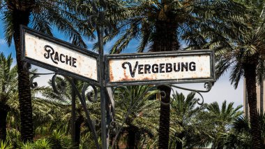 Almanca 'nın iki farklı yönünü gösteren işaret direği olan bir resim. Bir yön bağışlayıcılığı gösterir, diğeri intikamı..