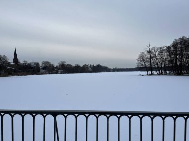 Akşam kış manzarası. Karların altında donmuş bir göl. Gri gökyüzü.