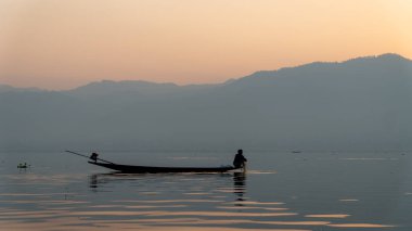 Inle Gölü, Myanmar - 12 Mart 2020: Balıkçı Inle Gölü kıyısında oturur ve tepede güneş doğarken elinde bir balık ağı tutar.