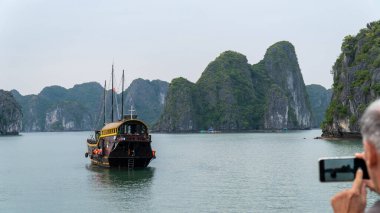 Halong Körfezi, Vietnam - 11 / 19 / 2019: Bir hurda teknesinin cep telefonuyla fotoğraf çeken adam.