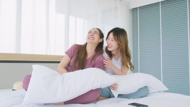 カジュアルな会話で美しいアジアの女性2人が 居心地の良いベッドルームのベッドの上に白い枕で座っている間 笑顔で楽しそうに笑っています 女の子に優しい友情 4Kリアルタイムビデオ — ストック動画