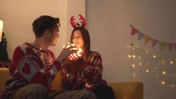 平安夜 穿着毛衣 在沙发上打杂灯笼的一对亚洲夫妇在家里客厅里一起玩球 在平安夜一起庆祝 — 图库视频影像