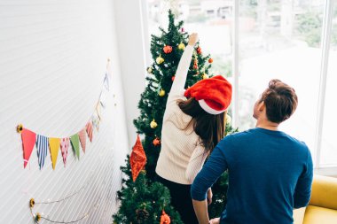 Mutlu genç çiftin sırtında süveter giyip evdeki oturma odasındaki Noel ağacında çeşitli takılar süslerken eğleniyorlar. Noel tatilinin tadını çıkarıyor ve kutluyoruz.