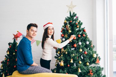Mutlu genç çift süveter giyip evdeki oturma odasındaki Noel ağacında çeşitli takılar süslerken eğleniyorlar. Noel tatilinin tadını çıkarıyor ve kutluyoruz.