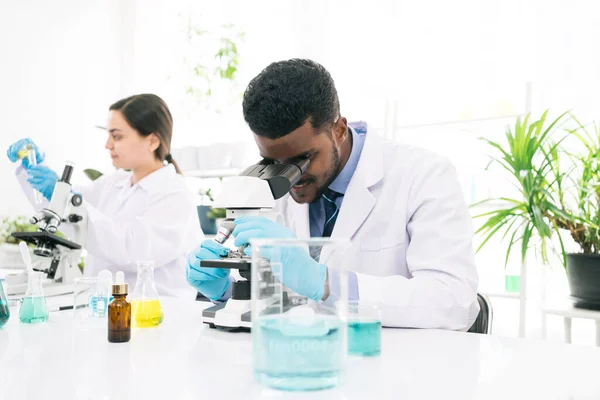 Young African black man scientist looking through a microscope in a laboratory for doing research. Students analyze biochemical by microscope research in the lab for discovering new medicine.