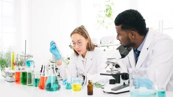 Caucasian woman and African black man scientists researchers use a lab dropper to drip a substance into a graduated cylinder for analysis of liquids in the lab. Diversity of scientists in the lab.