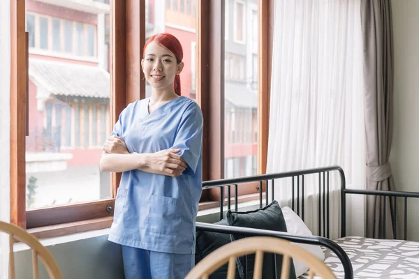 Portrait of Asian therapist woman nurse wearing medical scrubs in the house of patient. Caregiver visit at home. Home health care and nursing home concept.