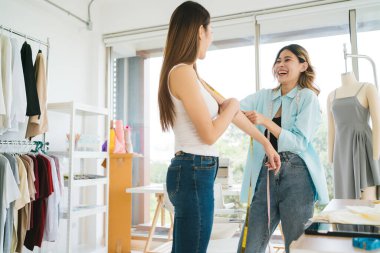 Asyalı kadın terzi yeni kıyafetler dikmek için müşterilerin vücutlarını ölçer. Atölye terzisi atölyesindeki müşteriler için yeni moda koleksiyonları tasarlayan çekici bayan moda tasarımcısı..