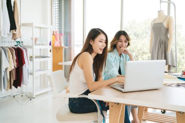 İki Asyalı moda tasarımcısı veya terzisi yeni koleksiyonun tasarımını dizüstü bilgisayarında kumaş ve çizim örnekleriyle tartıştılar. Stüdyoda birlikte çalışıyoruz..