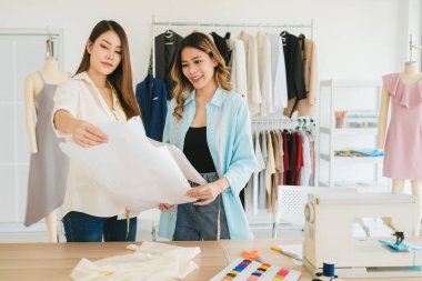 Asyalı kadın moda tasarımcısı ya da terzi kesik kağıt kumaş kalıplarını hazırlamaya yardım ediyor. Atölye terzi atölyesinde çalışan ve yeni moda koleksiyonları tasarlayan bir terzi..