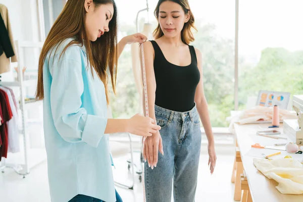 Asian woman tailor measures customers' bodies to make new clothes. Attractive female fashion designer dressmaker working and designing new fashion collections for customers in atelier tailor workshop.