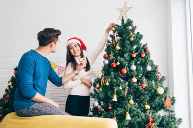 Mutlu genç çift süveter giyip evdeki oturma odasındaki Noel ağacında çeşitli takılar süslerken eğleniyorlar. Noel tatilinin tadını çıkarıyor ve kutluyoruz.