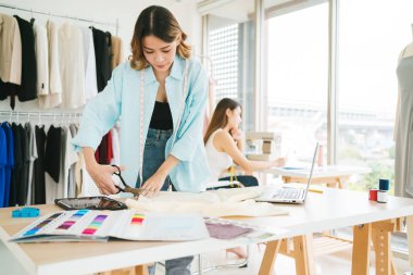 Asyalı kadın terzi ya da moda tasarımcısı elbise deseni yapmak için makasla kumaş kesiyor. Moda tasarımcısı ya da atölyedeki lağım temizleyicisi yeni koleksiyon giysileri için çalışıyor..