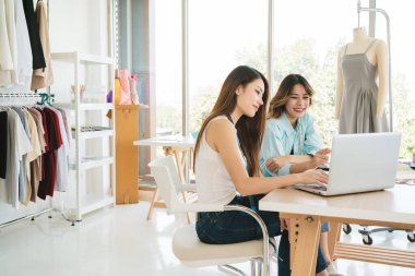 İki Asyalı moda tasarımcısı veya terzisi yeni koleksiyonun tasarımını dizüstü bilgisayarında kumaş ve çizim örnekleriyle tartıştılar. Stüdyoda birlikte çalışıyoruz..