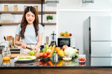 A happy young Asian woman preparing a healthy salad with fresh vegetables on a cutting board in the home kitchen. Food cooking for couple husband and wife in a good relationship.