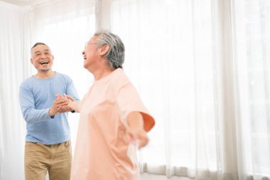 Romantik ve neşeli Asyalı son sınıf çifti dans etmekten ve müziğe el ele tutuşmaktan keyif alır. Oturma odasında gülümseme ve mutlulukla birlikte. Evde yaşlılar için emeklilik etkinliği.