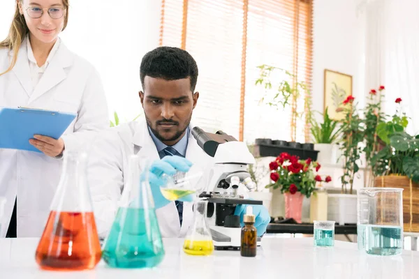 Diversity scientists: Black scientist pouring liquid with a Caucasian female scientist at the back in a research laboratory. Chemistry students working in the laboratory with microscope and beakers.