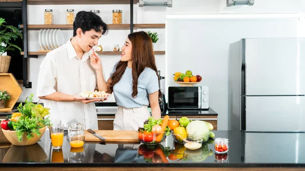 A happy couple prepares and cooks healthy salad with vegetables on a cutting board together in the home kitchen. Food cooking for young couple husband and wife in a good mood and healthy relationship.