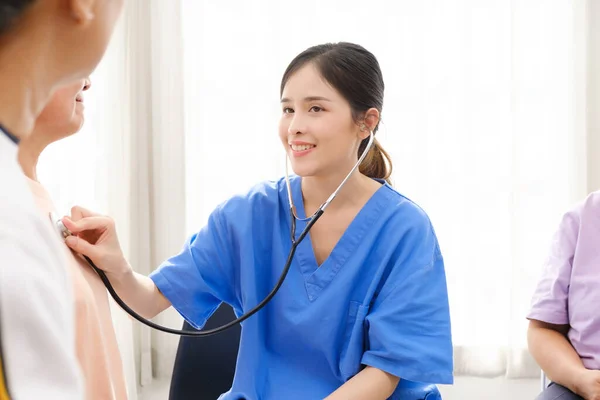 Asian nurse using a stethoscope for checking the heart rate of the senior female patient at home. Medical assistance . Caregiver nursing home concept.
