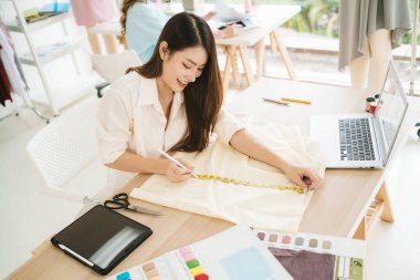 Asyalı kadın moda tasarımcısı ya da terzi el ölçü kağıdıyla kıyafet deseni yapmak için mezurayı ölçüyor. Moda tasarımcısı atölyede yeni bir koleksiyon için çalışıyor..