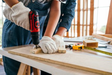 Asian father and son work as a woodworker or carpenters. Close up hands of the father and his son drill holes in a wooden plank carefully together. carpentry working at a home workshop studio.