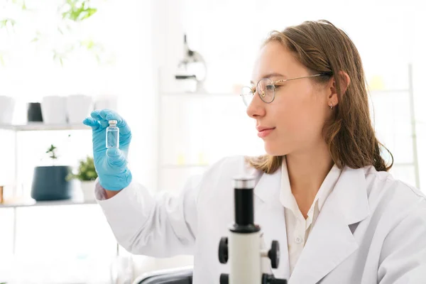 Caucasian woman scientist researcher looking and holding a small Medium glass bottle for chemical analysis of liquids in the lab. Scientist working with chemical equipment in the lab.