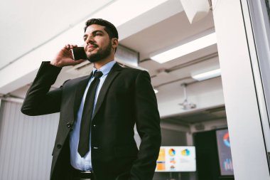 Smart and positive businessman calling and talking on smartphone alone in the office. Professional making business calls on the phone and enjoying corporate mobile conversation indoors.