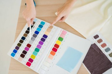 Colorful sample fabrics catalog palette with a pointer hand and pencil of the designer. Sample materials for dressmakers working on new collections for customers in an atelier tailor workshop.