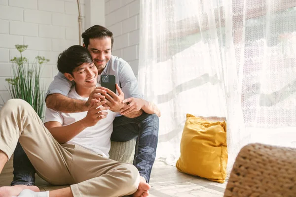 Caucasian Asian Lgbt Couple Embracing Back Sitting Using Smart Phone — Stock Photo, Image