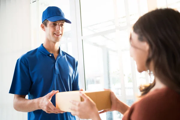 stock image Caucasian man courier in uniform delivering a parcel shipping package to customer Asian woman hands to hand in front of the entrance door at home. Home parcel shipping delivery service concept.