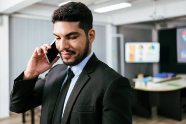 Akıllı ve pozitif iş adamı ofiste tek başına arıyor ve akıllı telefondan konuşuyor. Profesyonel iş görüşmeleri yapıyor ve şirket içi cep telefonu konuşmalarının tadını çıkarıyor..