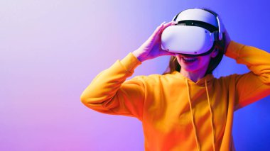 Sarı kapüşonlu ve VR kulaklık takan beyaz güzel bir kadın arka planda kırmızı ve mavi bir ışık, fütüristik teknoloji ve giyilebilir cihaz konseptiyle sanal gerçeklik yaşıyor.