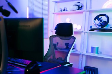 Profesyonel bir oyuncu için karanlık oda rahat bir oyun koltuğu, bilgisayar masası, neon ışıklar, klavye, monitör, kumanda ve mikrofon ile podcast kaydetmek ve evde canlı yayın.