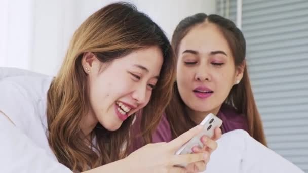 快乐的亚洲女性情侣们用智能手机躺在床上 用手指触摸屏幕 女性使用社交网络 聊天或从智能手机上进行网上购物的工具 — 图库视频影像