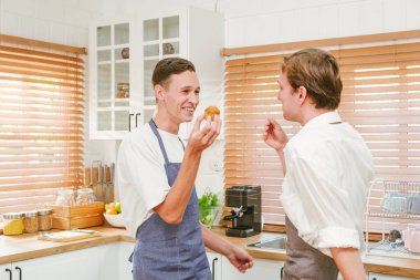 Önlük takan, gülümseyen ve yemek pişirmekten zevk alan beyaz eşcinsel çiftin portresi. Evdeki mutfakta birinin yüzünde un lekesi vardı. LGBT ilişkisi. Eşcinsel çift yemek pişirme konsepti.