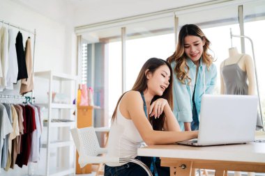 İki Asyalı moda tasarımcısı veya terzisi yeni koleksiyonun tasarımını dizüstü bilgisayarında kumaş ve çizim örnekleriyle tartıştılar. Stüdyoda birlikte çalışıyoruz..