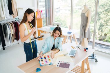 İki Asyalı moda tasarımcısı veya terzisi yeni koleksiyonun tasarımını dizüstü bilgisayarında kumaş ve çizim örnekleriyle tartıştılar. Stüdyoda birlikte çalışıyoruz..