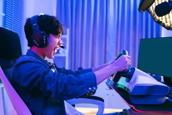 Asian male pro gamer playing an online car drive simulation game with steering wheel controller. Gamer winning an esports game with victory emotion. The player rejoices in victory in the competition.