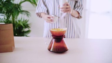 Cam damlatıcısının üzerindeki kağıt filtreye kahve dökmeden önce kağıt filtreye güzel kahve koyan bir kadının ekili videosu. Alternatif yöntemin adı Damlatma.