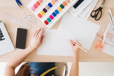 Kadın moda tasarımcısının ya da terzinin ellerinin masa üzerinde kumaş örnekleri olan yeni tasarım koleksiyonunu kağıda çizerken üst görüntüsü. Moda tasarımcısı küçük bir iş konsepti üzerinde çalışıyor..