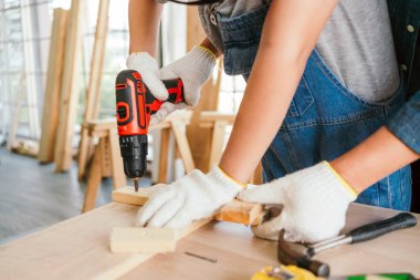 Asian father and son work as a woodworker or carpenters. Close up hands of the father and his son drill holes in a wooden plank carefully together. carpentry working at a home workshop studio.