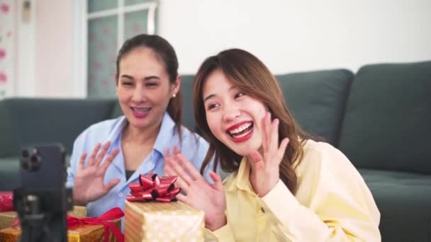 陽気な2人のアジアの女性ブロガーは スマートフォンやラップトップを介してソーシャルメディア上のライブストリームで自宅で顧客のための自信を持っていくつかのランダムなギフトボックスを販売しています ショッピングオンラインコンセプト — ストック動画