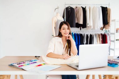 Güzel Asyalı kadın moda tasarımcıları veya terziler yeni koleksiyonun tasarımını kağıt üzerinde kumaş ve eskiz örnekleriyle yapıyor. Moda tasarımcısı stüdyoda çalışıyor. Küçük işletme kavramı.