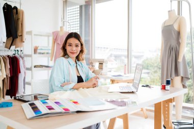 Güzel Asyalı kadın moda tasarımcıları veya terziler yeni koleksiyonun tasarımını kağıt üzerinde kumaş ve eskiz örnekleriyle yapıyor. Moda tasarımcısı stüdyoda çalışıyor. Küçük işletme kavramı.