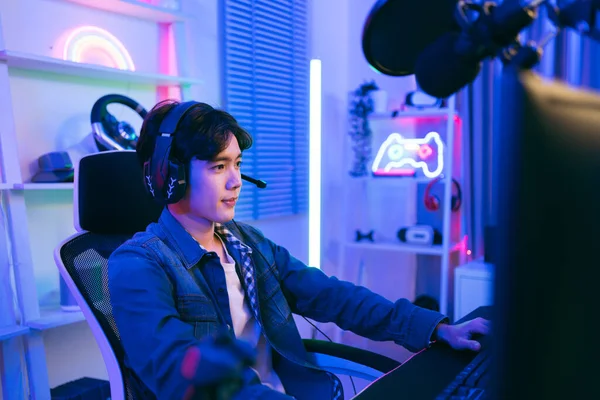 ジーンズジャケットを着た若いアジアの男性プロゲーマーは キーボード モニター マイクを備えたゲームテーブルで椅子に座っています 競争の準備 キャストゲームプレイやポッドキャストを記録 — ストック写真
