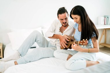 Kafkasyalı çiftin müzikle eğlenmesine bayılıyorum. Bir erkek, yatak odasında bir kadına ukulele çalmayı öğretiyor. Kopyalama alanı olan resim.